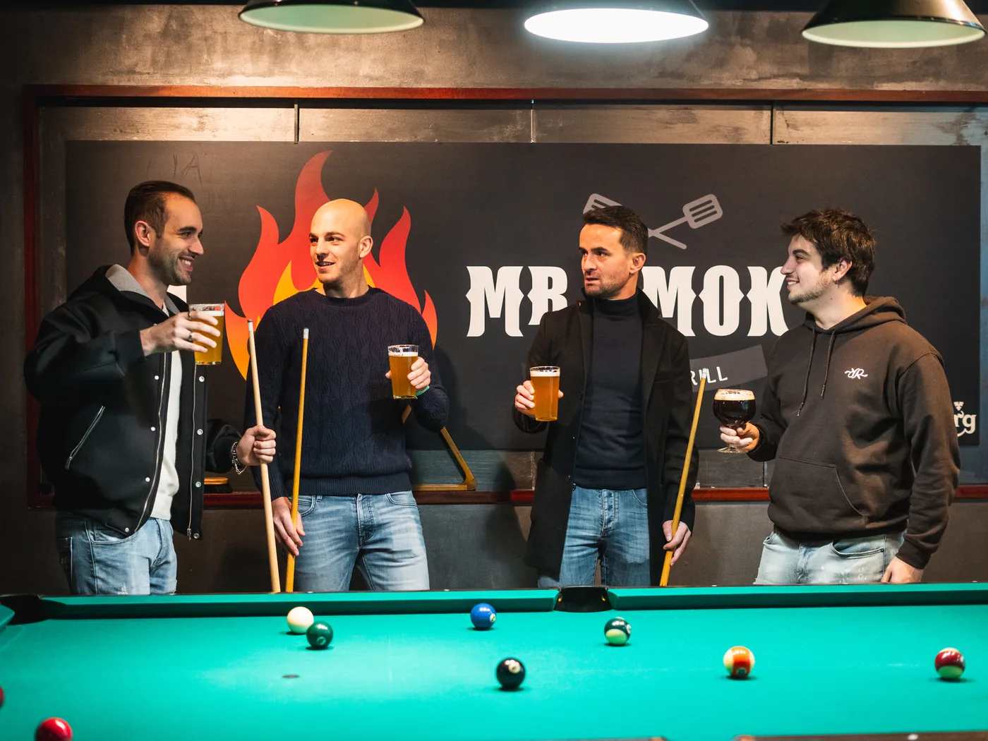 Quattro amici con la birra in mano attorno al tavolo da biliardo, nella sala sul retro